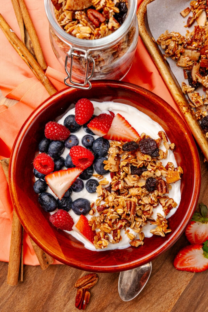 Homemade granola on a yogurt base with fresh fruit surrounding it in a wooden bowl.