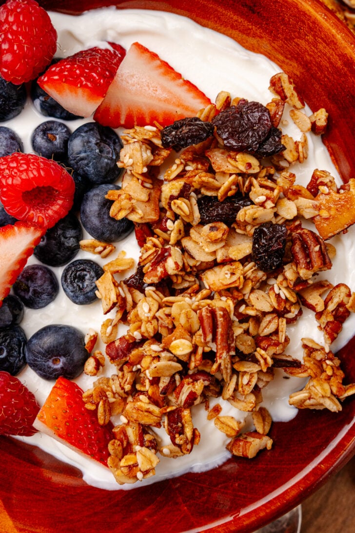 Homemade granola on a yogurt base with fresh fruit surrounding it in a wooden bowl.
