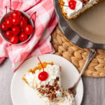 Million Dollar Pie slice on white plate with whipped cream, pecans, and maraschino cherry garnish, overhead view