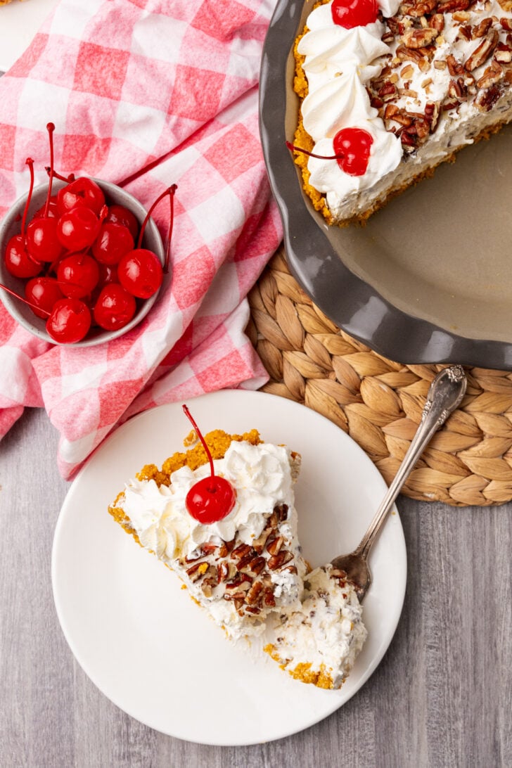 Million Dollar Pie slice on white plate with whipped cream, pecans, and maraschino cherry garnish, overhead view