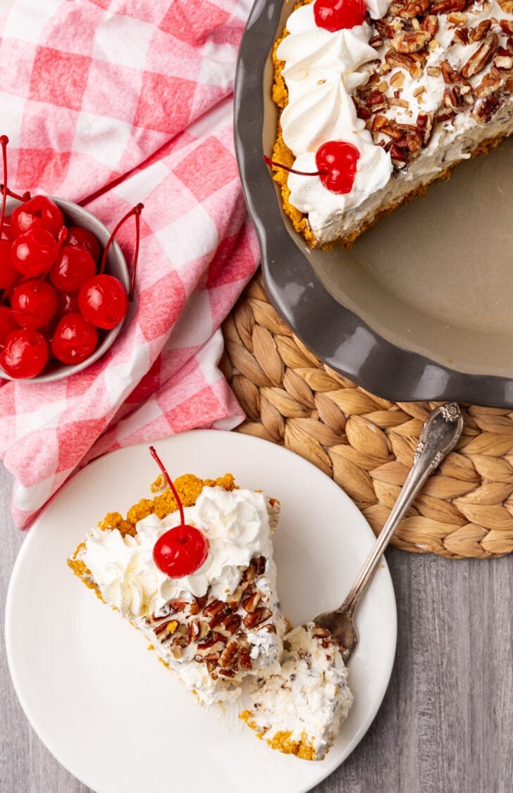 Slice of million dollar pie on a white plate topped with whipped cream and a cherry.