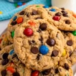 Stack of Monster Cookies loaded with colorful M&Ms and chocolate chips, with a container of candies blurred in the background