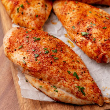 Roasted Chicken Breasts seasoned with paprika and black pepper, garnished with fresh chives, served on parchment paper on a wooden cutting b