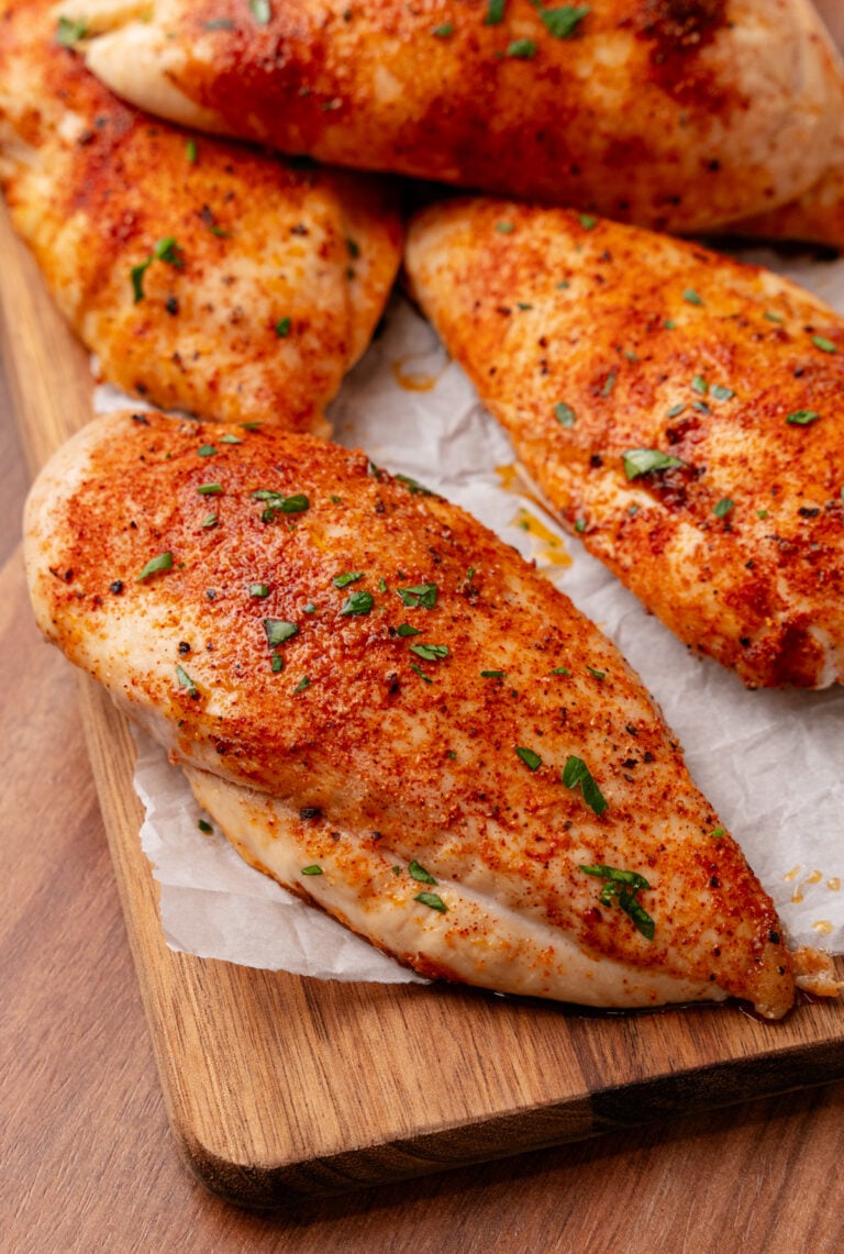 Roasted Chicken Breasts seasoned with paprika and black pepper, garnished with fresh chives, served on parchment paper on a wooden cutting b