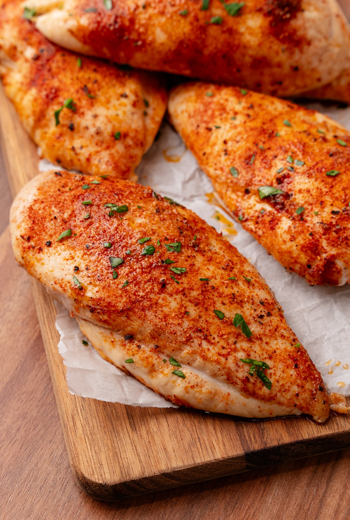 Roasted Chicken Breasts seasoned with paprika and black pepper, garnished with fresh chives, served on parchment paper on a wooden cutting b