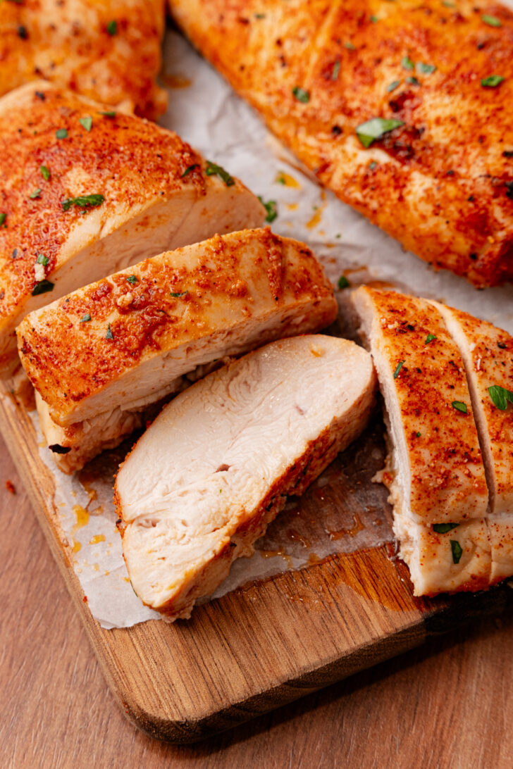 Sliced roasted chicken breasts on a wooden cutting board lined with parchment.