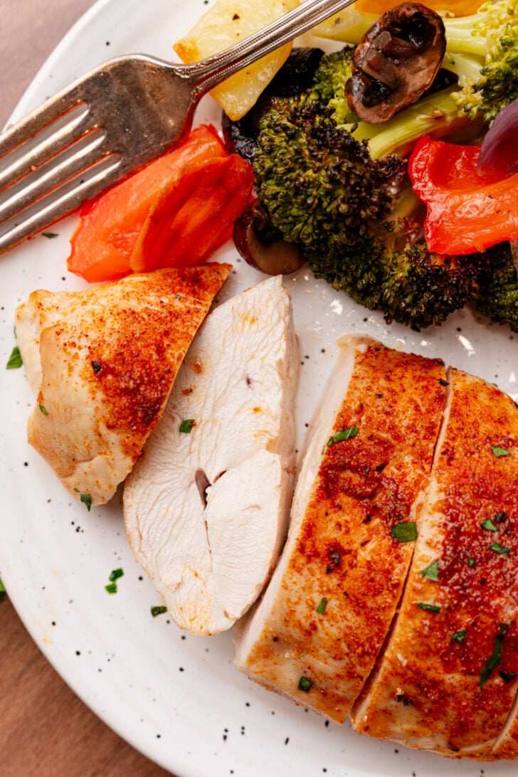 Sliced roasted chicken breasts on a white plate served with roasted vegetables.