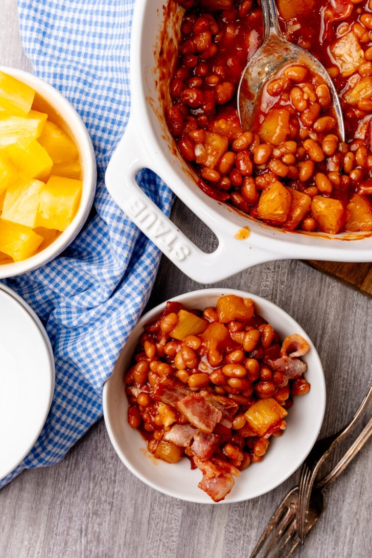 White dish of pineapple baked beans along with a casserole dish of baked beans.