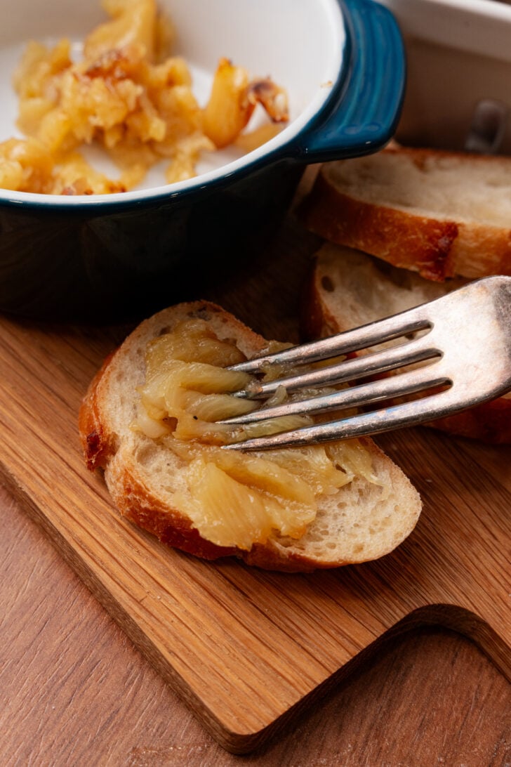 Roasted garlic clove smeared on toasted bread with a silver fork.