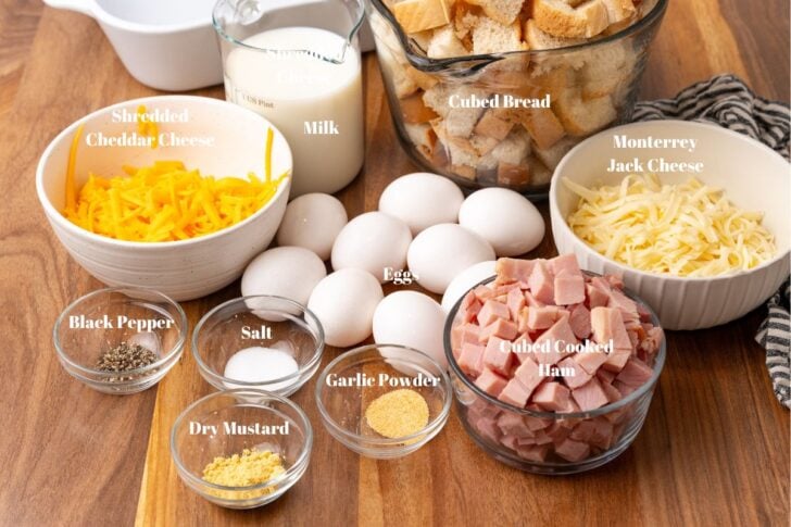 Ingredients for ham and cheese strata in clear glass bowls with a large white bowl for mixing.