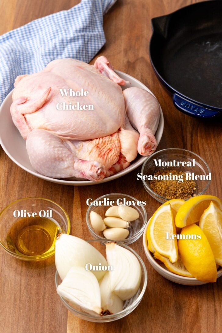 Whole chicken and other ingredients in glass contains with a cast iron skillet for roasted chicken recipe.