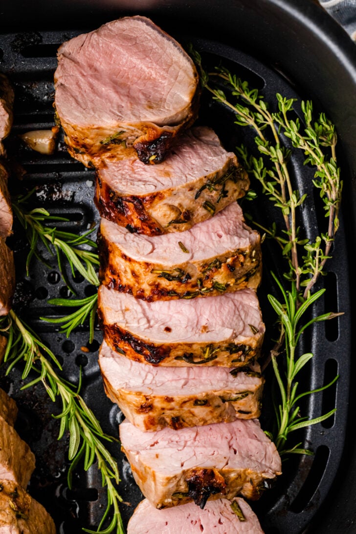 Sliced air fryer pork tenderloin served with fresh rosemary and thyme.