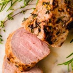 Air Fryer Pork Tenderloin (Juicy And Flavorful) sliced on marble with fresh rosemary garnish, showing pink interior and caramelized crust