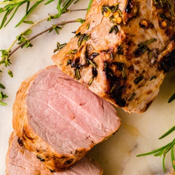 Air Fryer Pork Tenderloin (Juicy And Flavorful) sliced on marble with fresh rosemary garnish, showing pink interior and caramelized crust