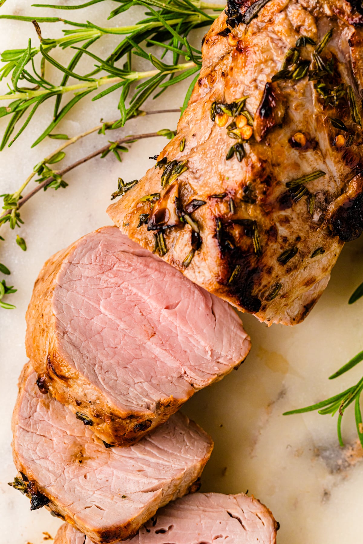 Air Fryer Pork Tenderloin (Juicy And Flavorful) sliced on marble with fresh rosemary garnish, showing pink interior and caramelized crust