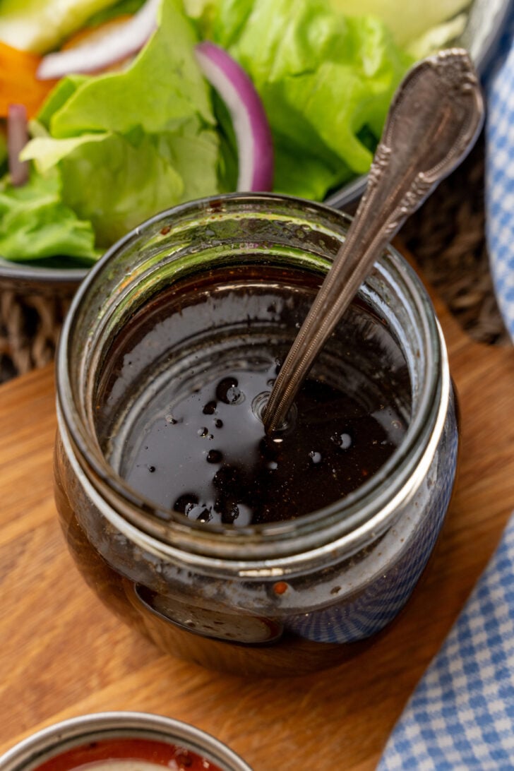 Small jar of balsamic vinaigrette dressing with a silve spoon for serving.