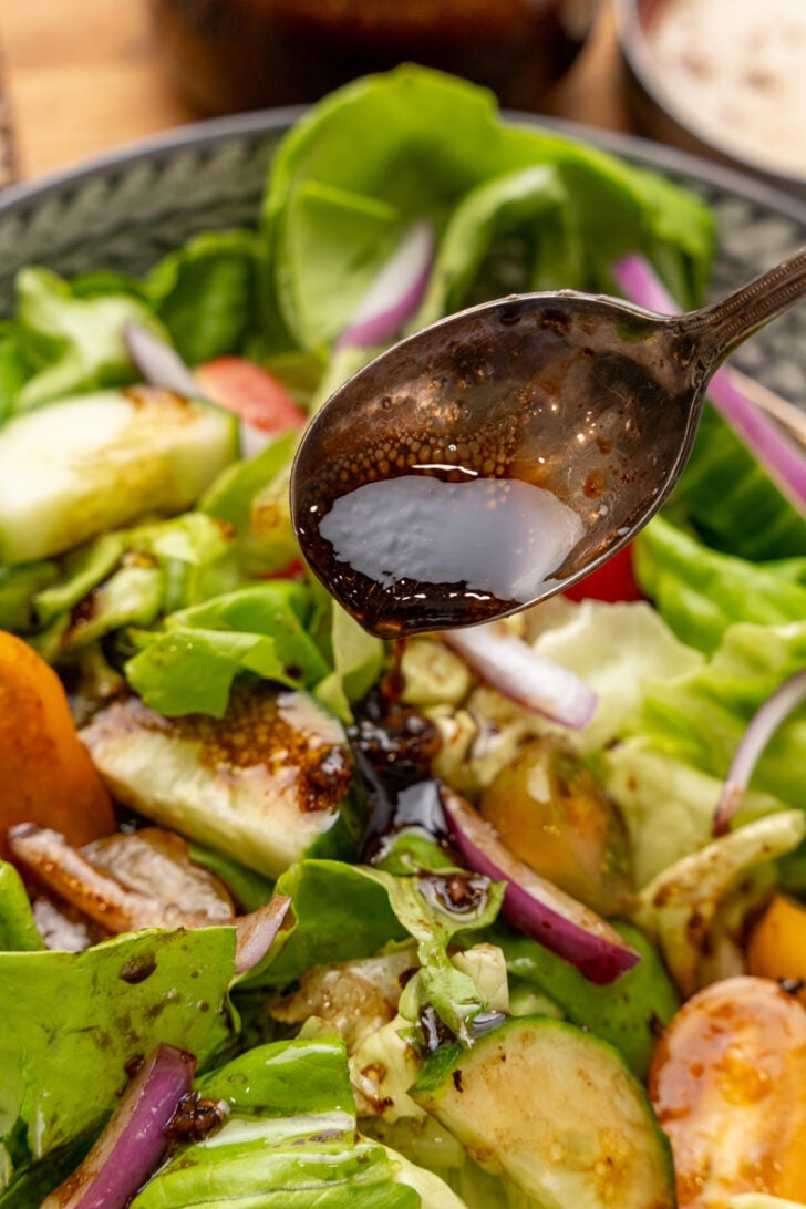 Silver spoon serving homemade balsamic dressing over a mixed green salad.