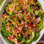 Easy BBQ Chicken Salad in white bowl with lettuce, shredded chicken, black beans, corn, crispy tortilla strips, red peppers, and creamy dres