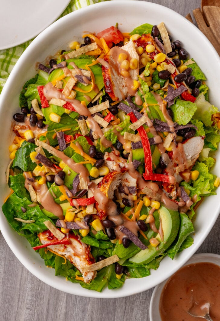 Easy BBQ Chicken Salad in white bowl with lettuce, shredded chicken, black beans, corn, crispy tortilla strips, red peppers, and creamy dres