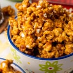 Easy Homemade Caramel Corn piled high in a colorful ceramic bowl with blue rim and green flower design, showing glossy caramel coating and w