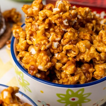 Easy Homemade Caramel Corn piled high in a colorful ceramic bowl with blue rim and green flower design, showing glossy caramel coating and w