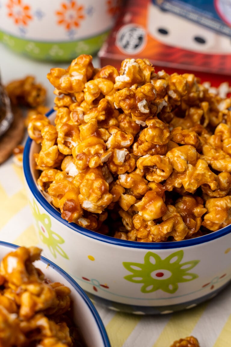 Easy Homemade Caramel Corn piled high in a colorful ceramic bowl with blue rim and green flower design, showing glossy caramel coating and w