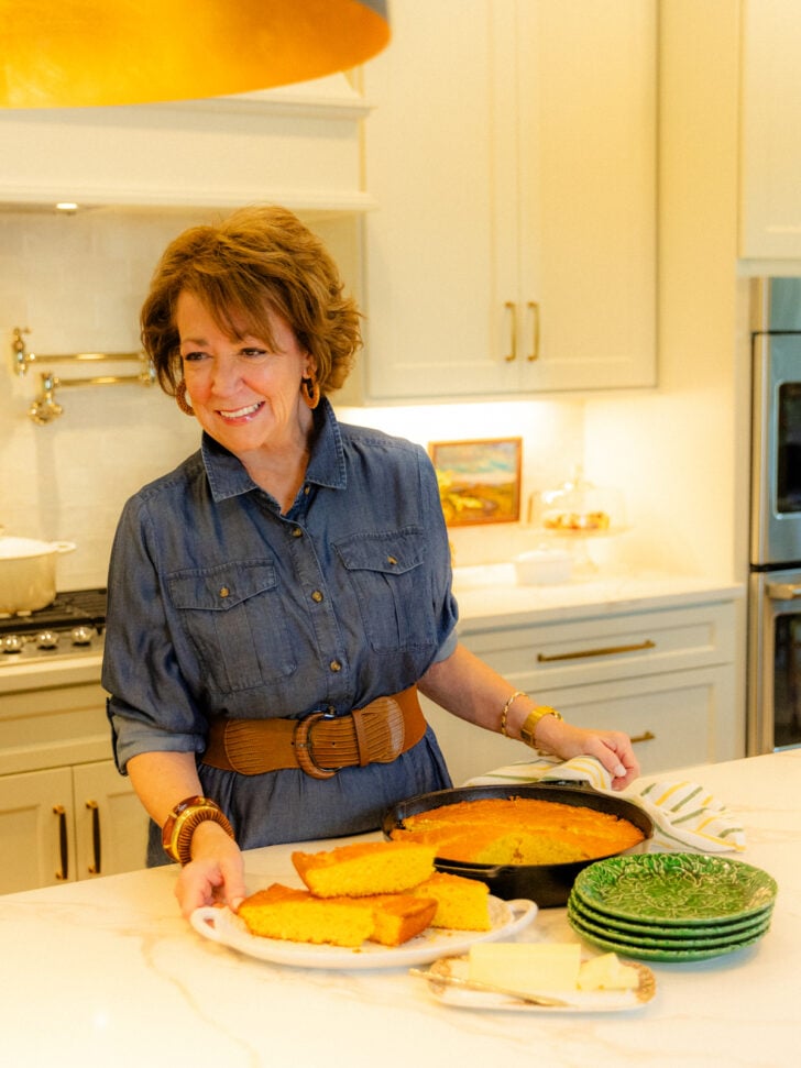 Woman in denim shirt at kitchen counter with cast iron skillet of cornbread and golden cornbread squares on plate, Beginners Guide To Cast I