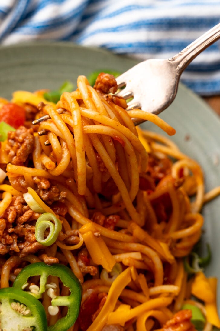 Fork serving a swirl of Cowboy spaghetti topped with green onions and sliced jalapenos.