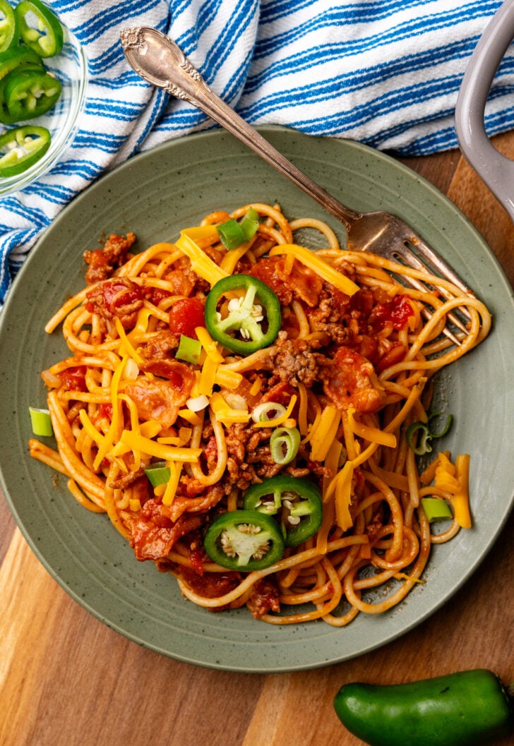 Green plate with large serving of Cowboy spaghetti topped with sliced jalapenos and green onions.