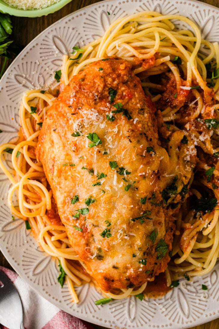 Crock Pot Chicken Parmesan with melted cheese and fresh parsley served over spaghetti on a decorative plate