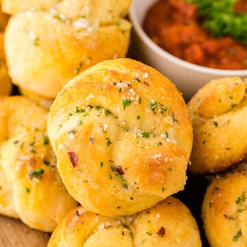 Golden garlic knots 7 1 topped with herbs and coarse salt, served with marinara sauce in a white bowl on wood