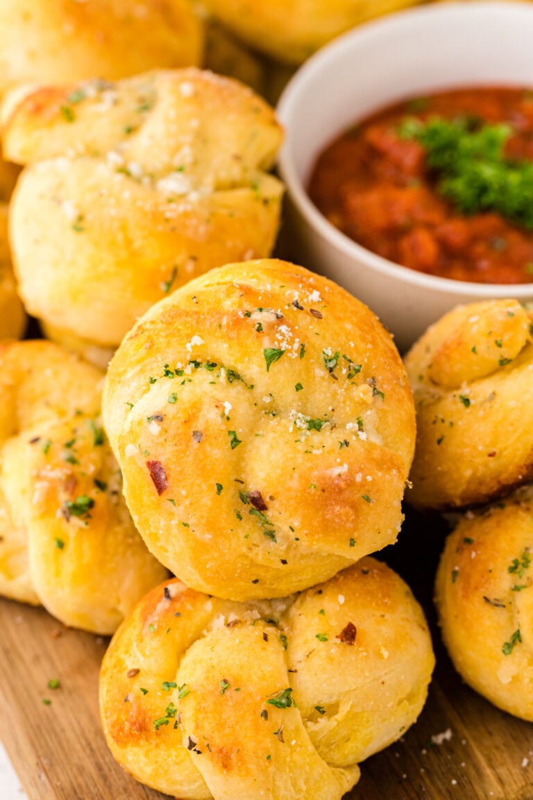 Golden garlic knots 7 1 topped with herbs and coarse salt, served with marinara sauce in a white bowl on wood