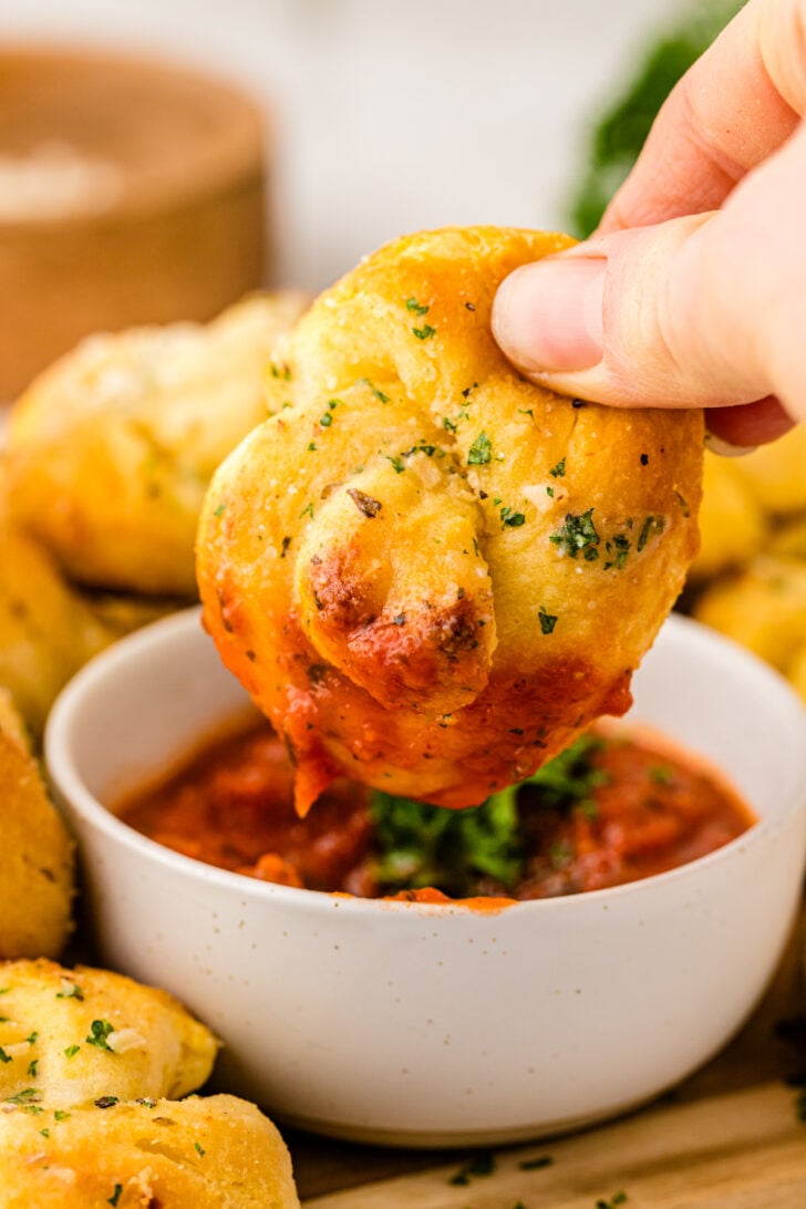Hand holding a garlic knot dipped into marinara sauce.