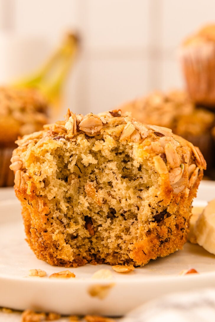 Granola Banana Muffin with a bite taken out sitting on a white plate.