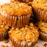 Stacked granola muffins 12 with sliced almonds on white plate, brown paper liners, close-up view
