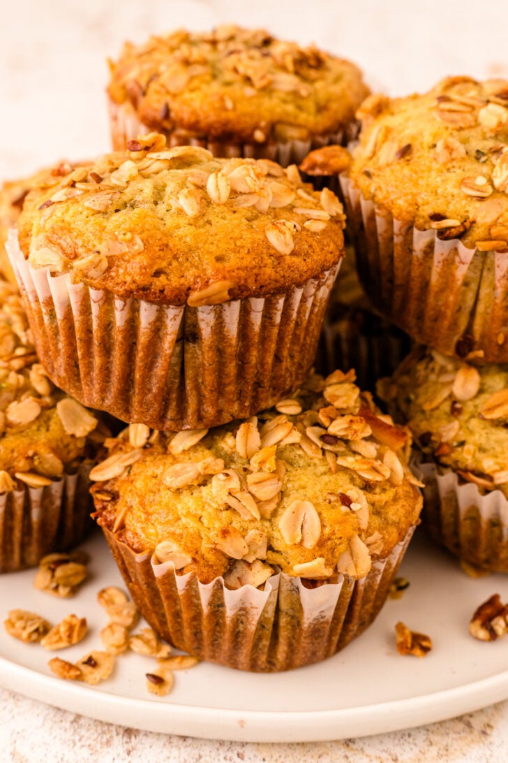 Stacked granola muffins 12 with sliced almonds on white plate, brown paper liners, close-up view