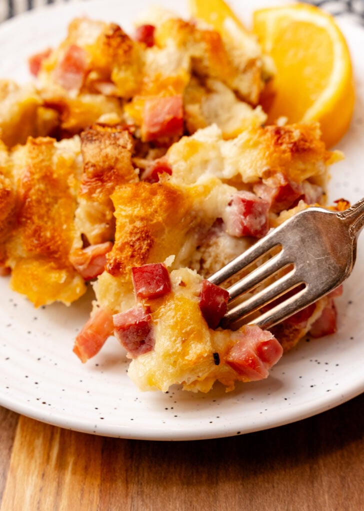White dish with a serving of ham and cheese strata with a silver fork.