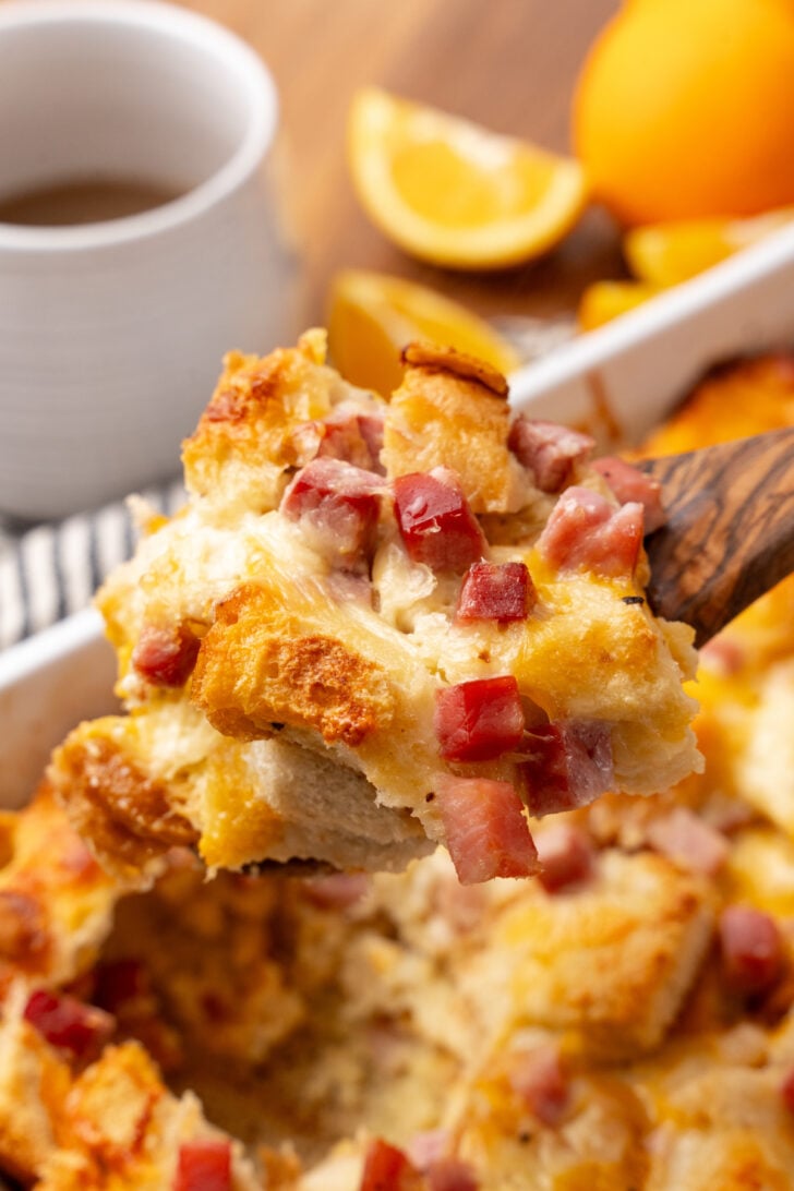 Wooden spoon holding scoop of ham and cheese strata.