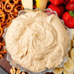 Peanut Butter Dip in a scalloped bowl surrounded by pretzels, strawberries, apples, and peanuts on a wooden board