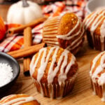 Glazed pumpkin muffins with white icing drizzle in paper liners on wood board with cinnamon sticks and fall decorations