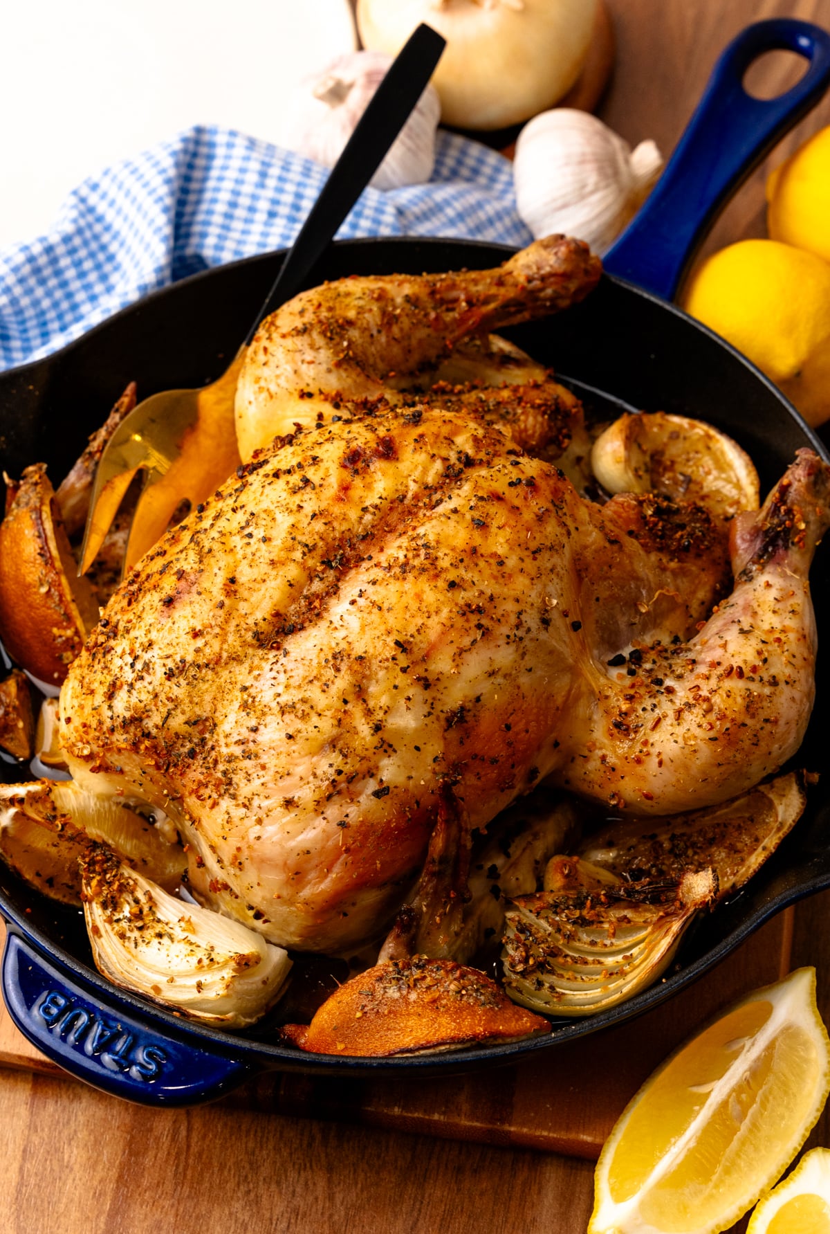 Roasted lemon chicken 4 in cast iron skillet with garlic, onions, and lemon wedges on wooden board