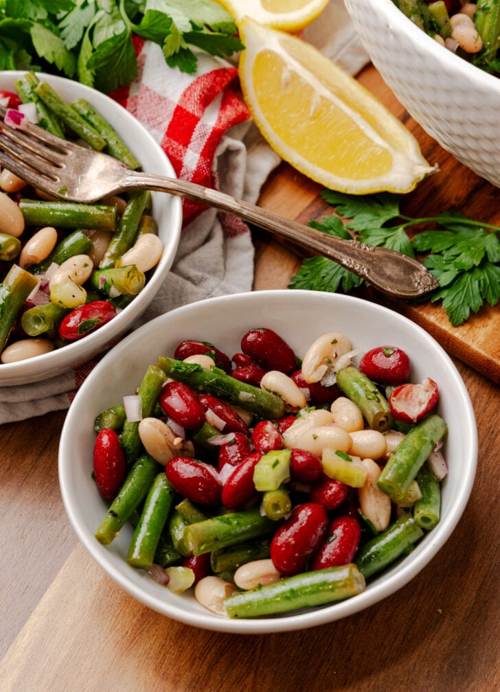 Three Bean Salad with green beans, white beans, and kidney beans in a light vinaigrette in white serving bowls.