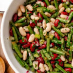 Three bean salad with green beans, white beans, and red peppers garnished with fresh parsley in a white speckled bowl