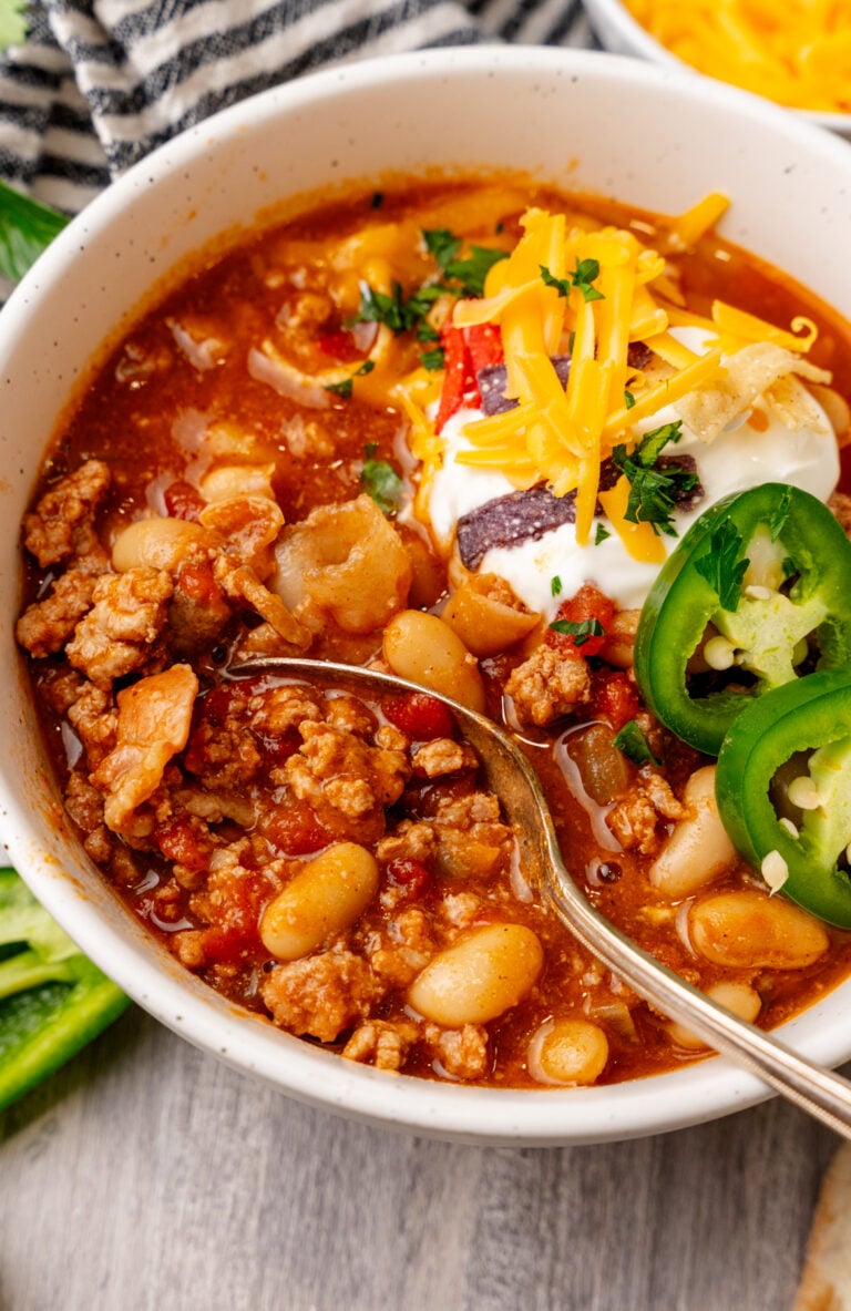 Turkey chili 12 in white bowl topped with sour cream, cheddar cheese, jalapeños, and cilantro with spoon