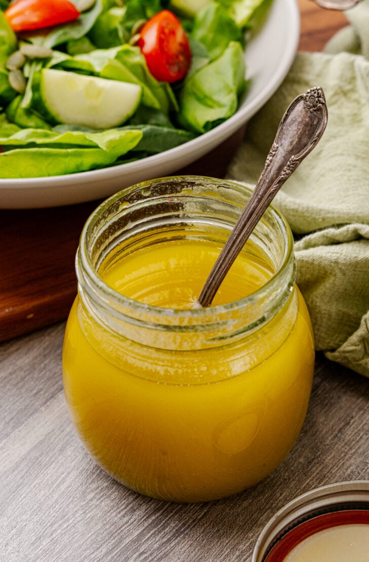 Small glass jar of homemade vinaigrette dressing served with a spoon.