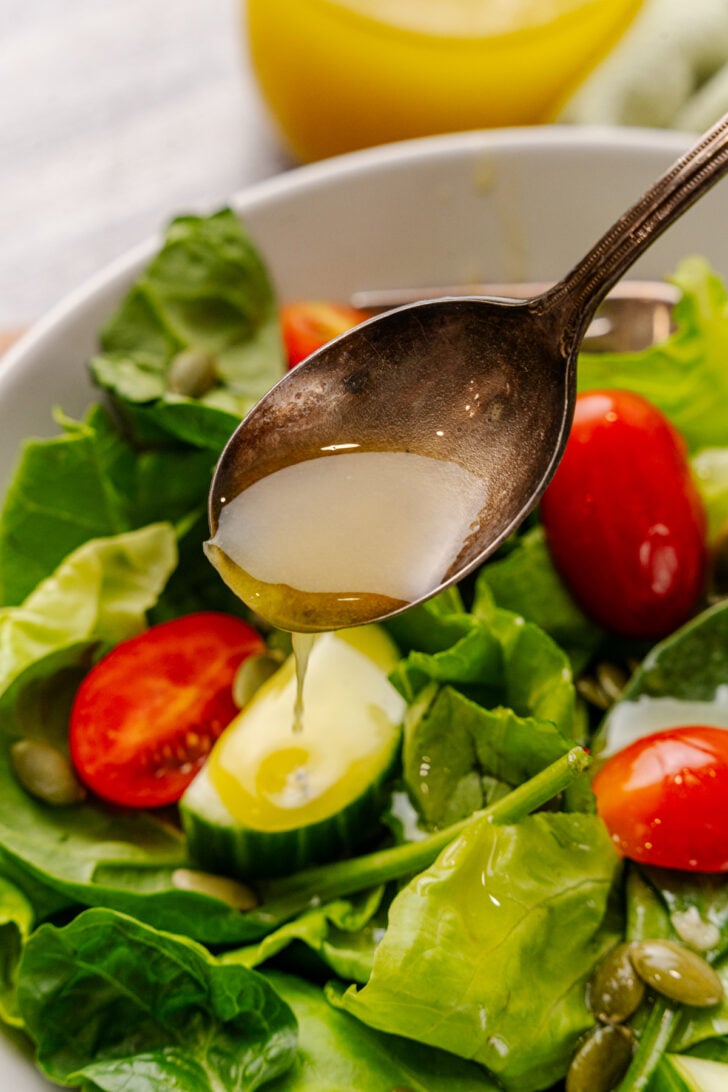 Spoonful of homemade dressing being drizzled on a fresh green salad.