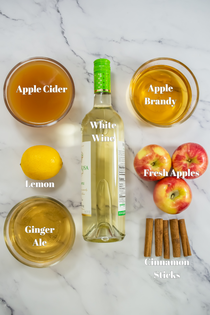 Ingredients for Apple Cider Sangria in glass containers on a marble counter.