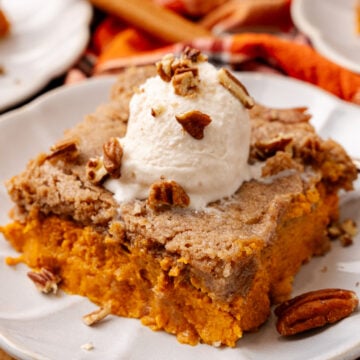 Pumpkin Spice Dump Cake topped with ice cream and chopped pecans served on a white plate.