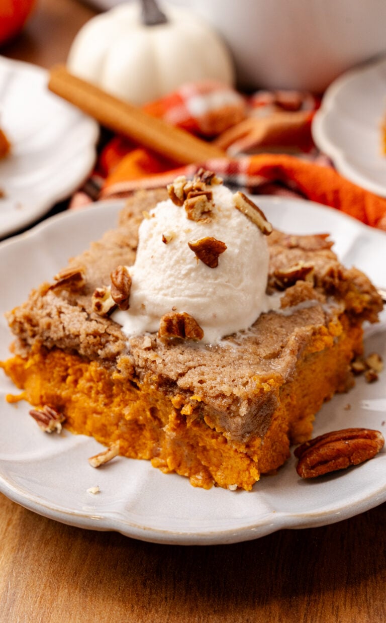 Pumpkin Spice Dump Cake topped with ice cream and chopped pecans served on a white plate.