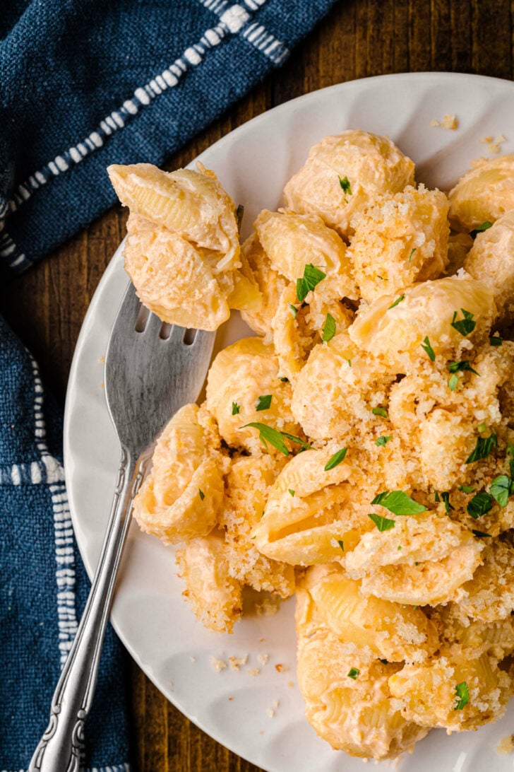 Easy Pasta Shells And Cheese served on white plate with fork, garnished with fresh parsley, overhead view on dark wood table